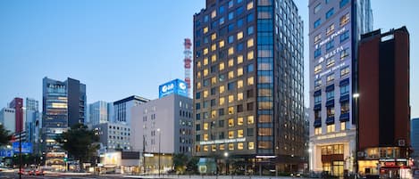 A modern hotel with a prominent glass facade, multiple floors, and illuminated signage.