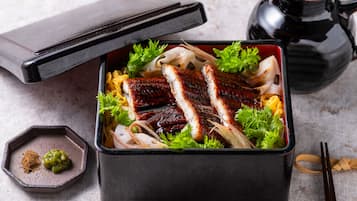 A traditional Japanese bento box with grilled fish, vegetables, and a small dish of sauce.