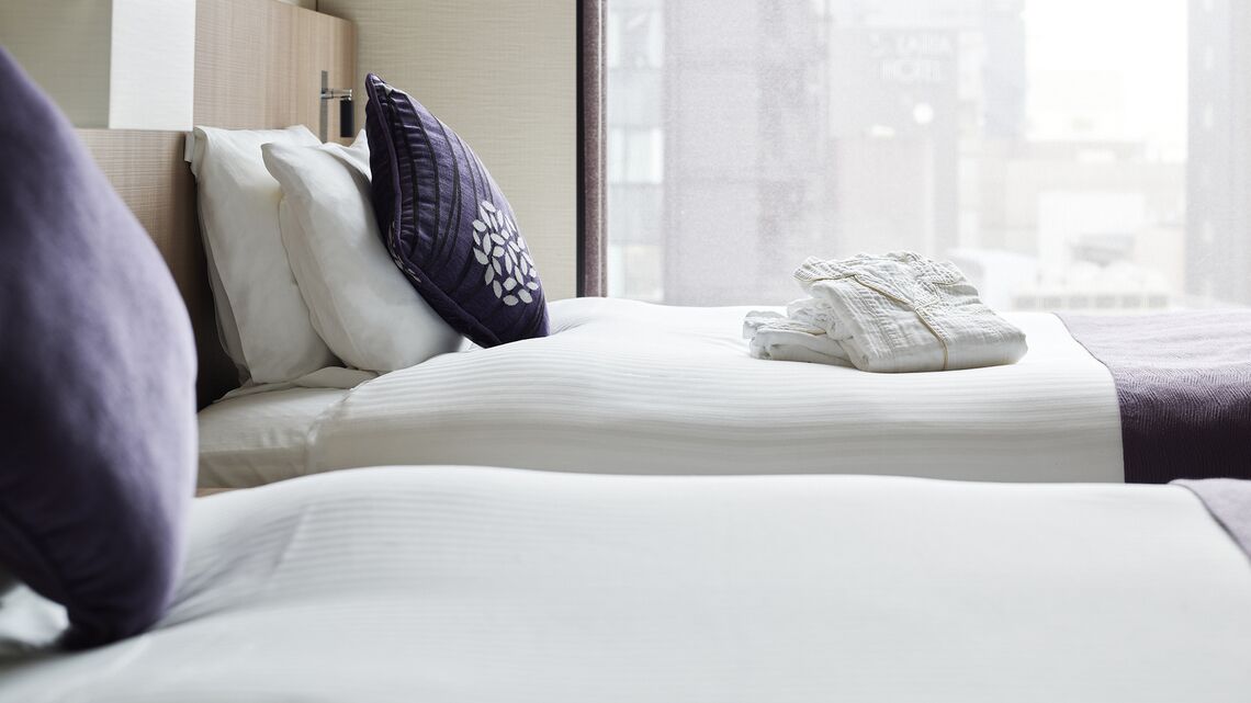 A hotel room with two beds, a window with a city view, and neatly folded towels on the bed.