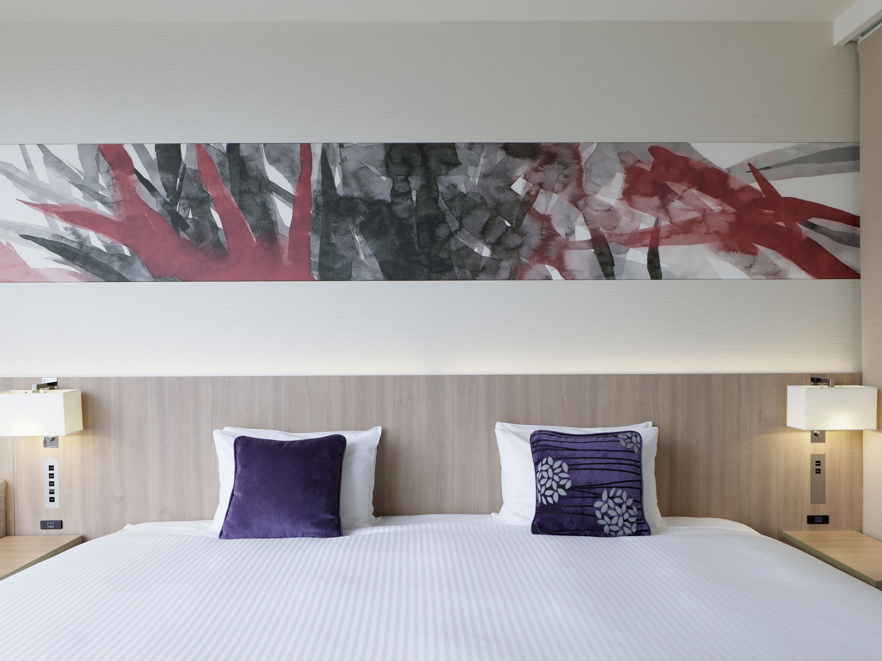 Une chambre d’hôtel avec un grand tableau abstrait, deux oreillers, un lit et des lampes de chevet.