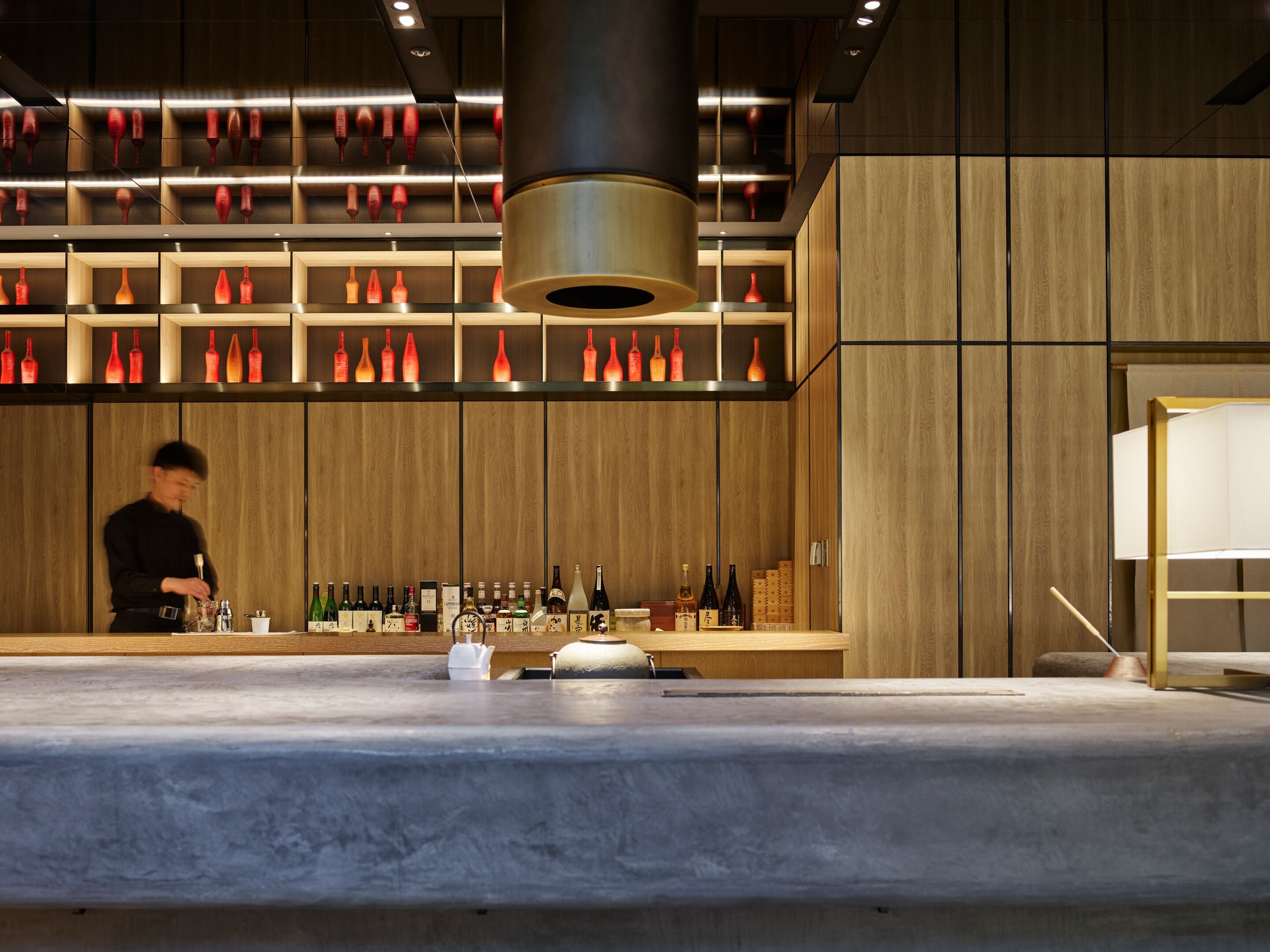 Un coin bar avec des lambris en bois, une variété de bouteilles et une personne qui prépare des boissons.