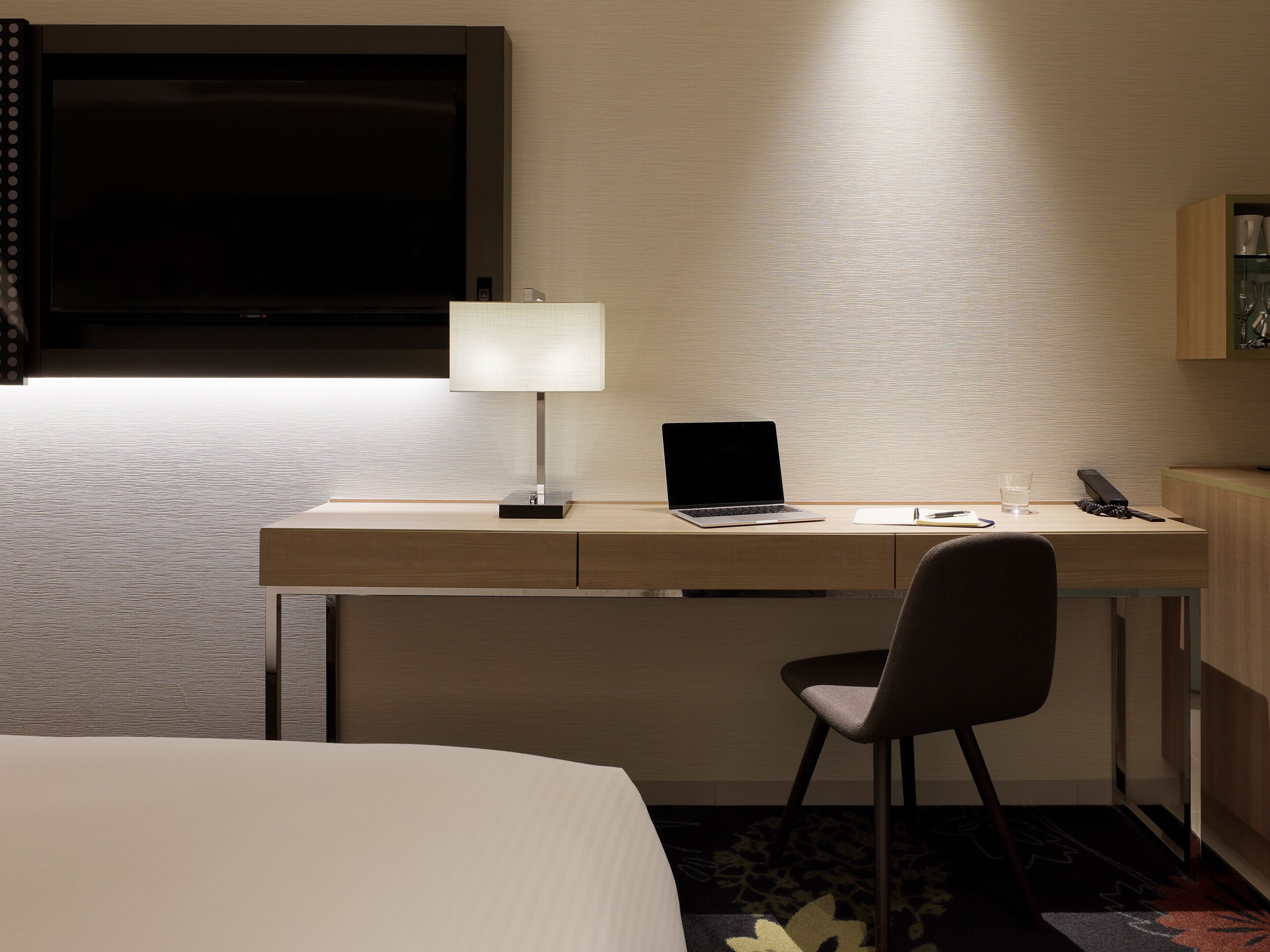 Habitación de hotel con escritorio, silla, ordenador portátil, lámpara y televisor.