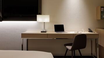 Habitación de hotel con escritorio, silla, ordenador portátil, lámpara y televisor.