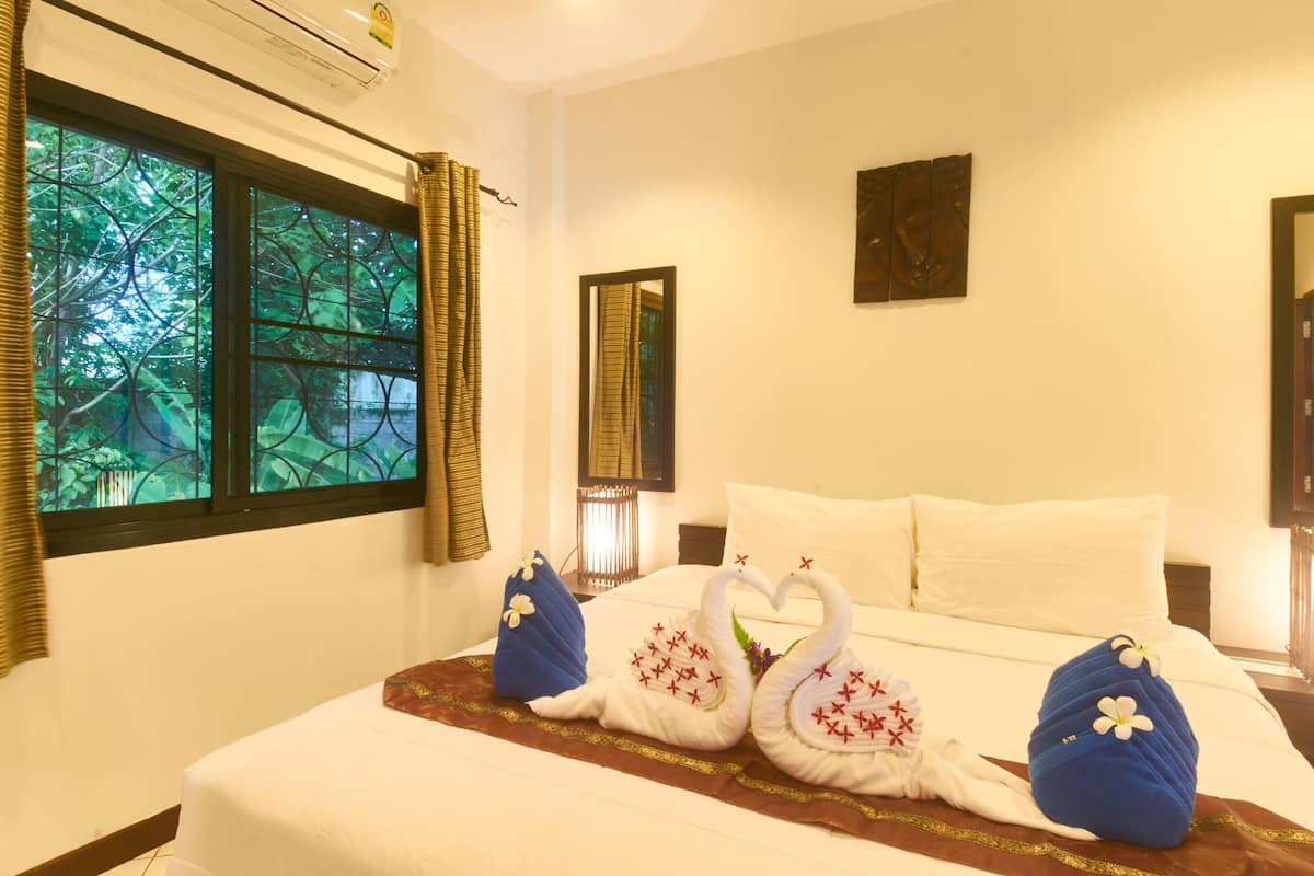 A hotel room with a bed, a window with curtains, a wall-mounted mirror, and a painting.