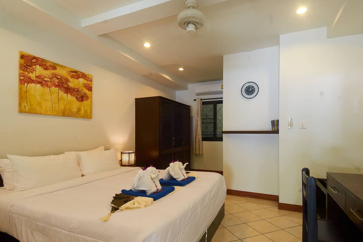 A hotel room with a bed, a painting, a wardrobe, a desk, and a clock on the wall.