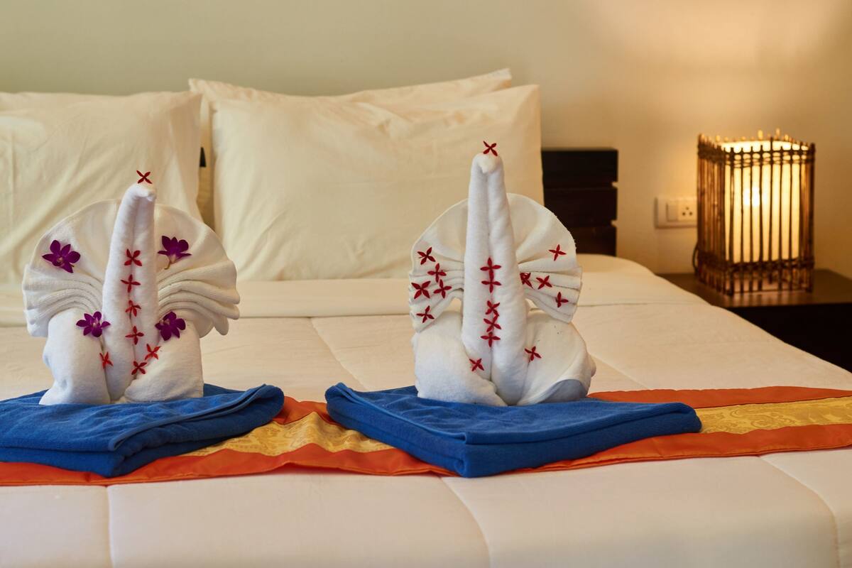 A neatly made bed with two decorative swan-shaped towels and a blue and orange towel on the bed.