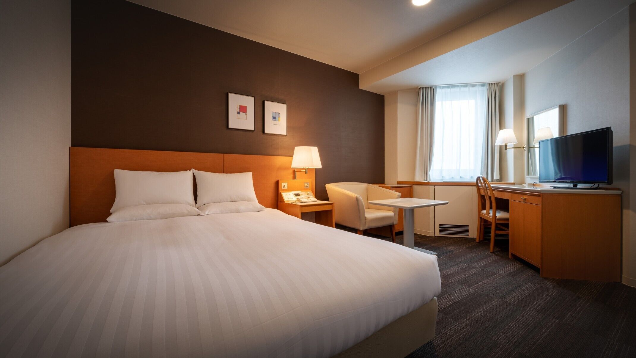 Une chambre d’hôtel avec un grand lit, un bureau avec une chaise, une télévision et deux tableaux encadrés au mur.