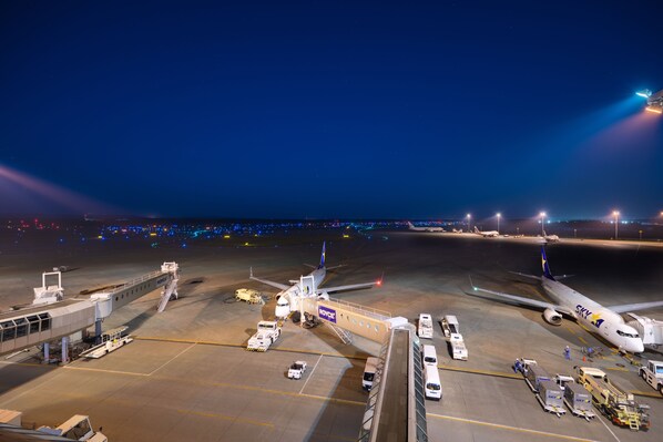 An airport tarmac at night with airplanes parked, ground support equipment, and a jet bridge connected to a terminal. - Air Terminal Hotel (Chitose)
