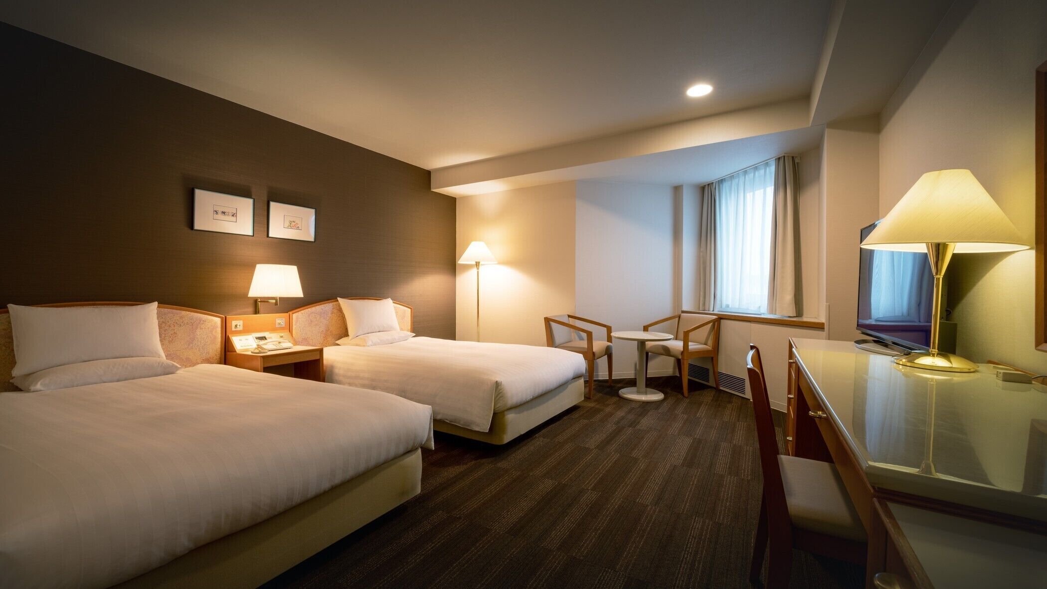 Une chambre d’hôtel avec deux lits, un bureau, une chaise, une télévision et une fenêtre avec des rideaux.
