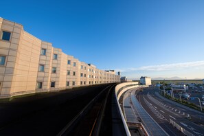 A modern building with a curved facade and a train track running alongside it. - Air Terminal Hotel (Chitose)