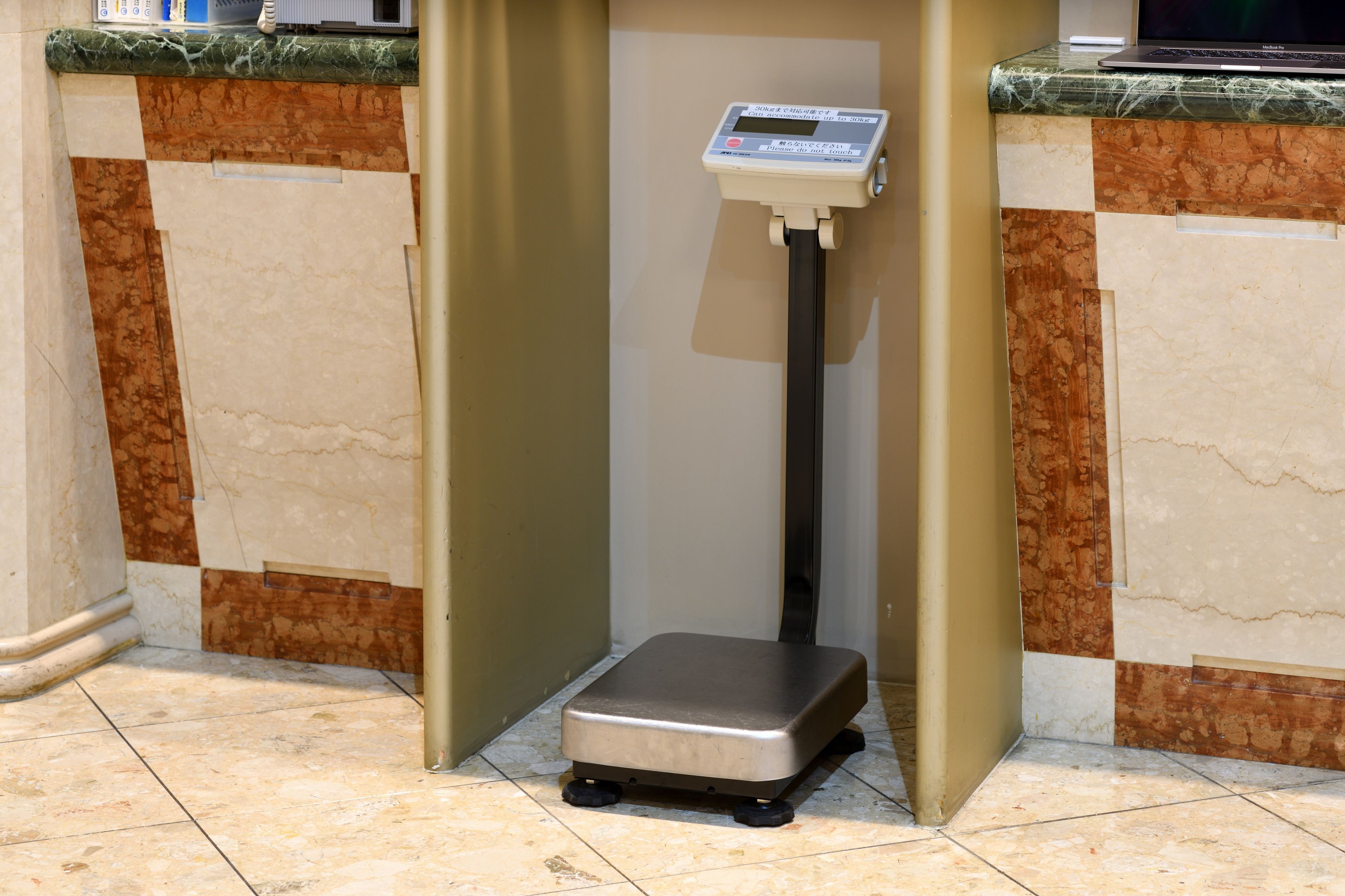 A weighing scale in a corner with a marble counter and a tiled floor.