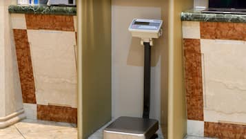 A weighing scale in a corner with a marble counter and a tiled floor.