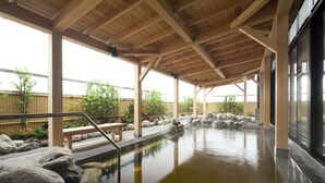 A covered outdoor hot spring area with wooden beams, a stone pathway, and a bench. - Air Terminal Hotel (Chitose)