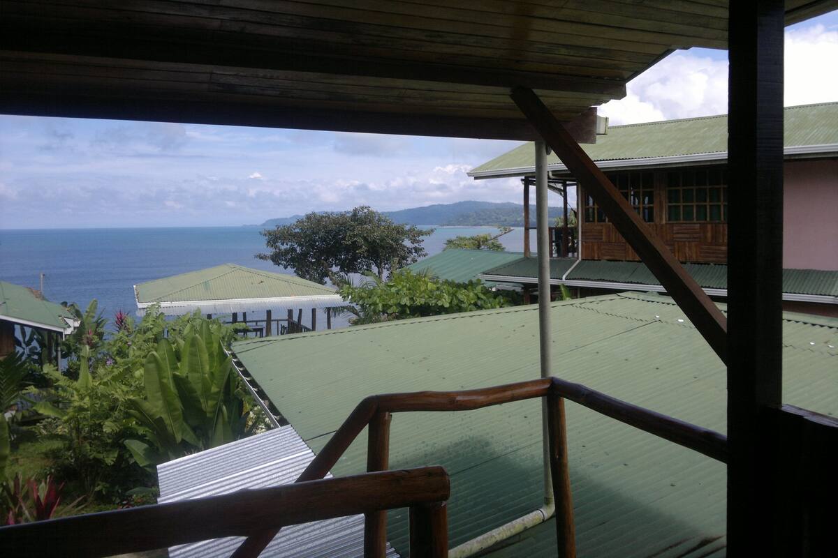 A wooden balcony overlooking a body of water with a view of the sea and distant mountains.