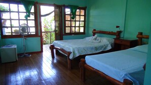 Une chambre avec deux lits en bois, un bureau en bois, une petite table, un ventilateur et un réfrigérateur.
