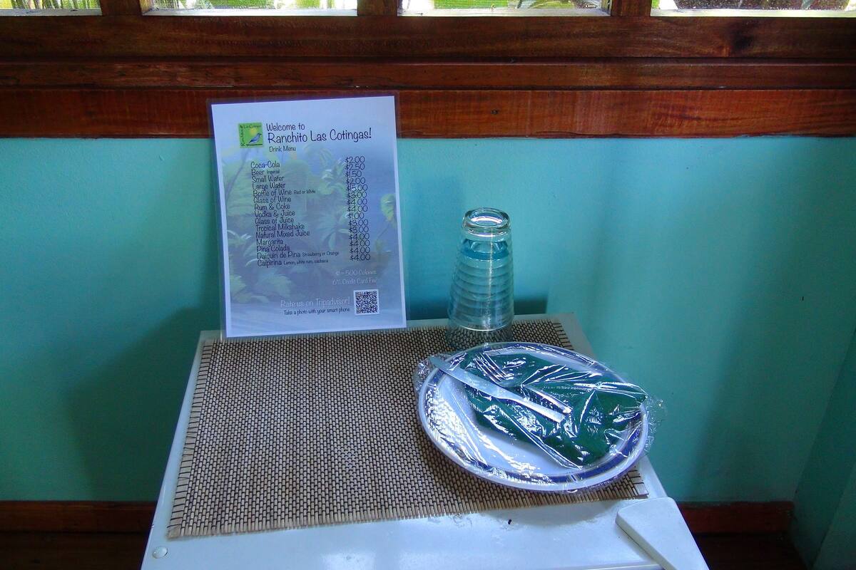 A drink menu on a table with a bottle and a plate of food.