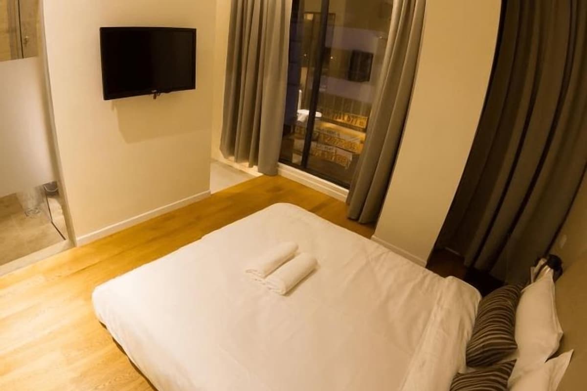 A hotel room with a bed, a flat-screen TV mounted on the wall, and a window with curtains.