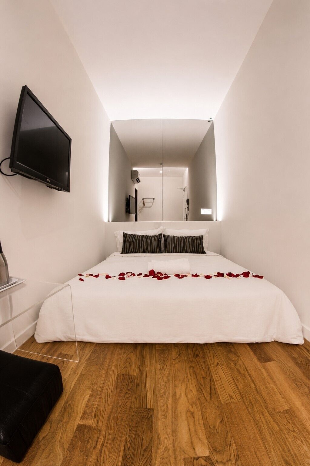Un dormitorio con una cama, un televisor montado en la pared y piso de madera.