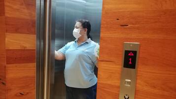 A person standing in an elevator with a wooden wall and a digital display showing the number 1.