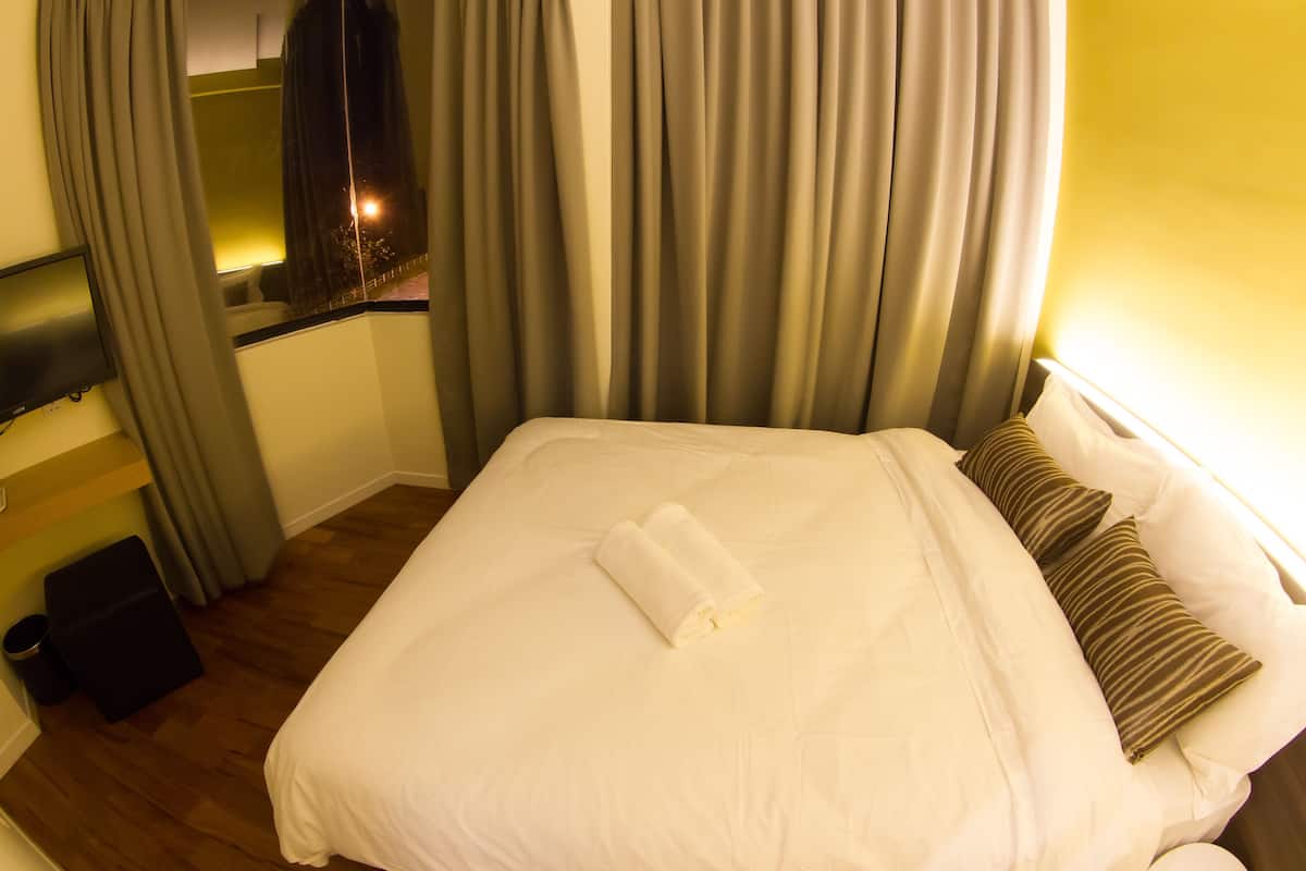 A hotel room with a bed, curtains, a TV, and a window.
