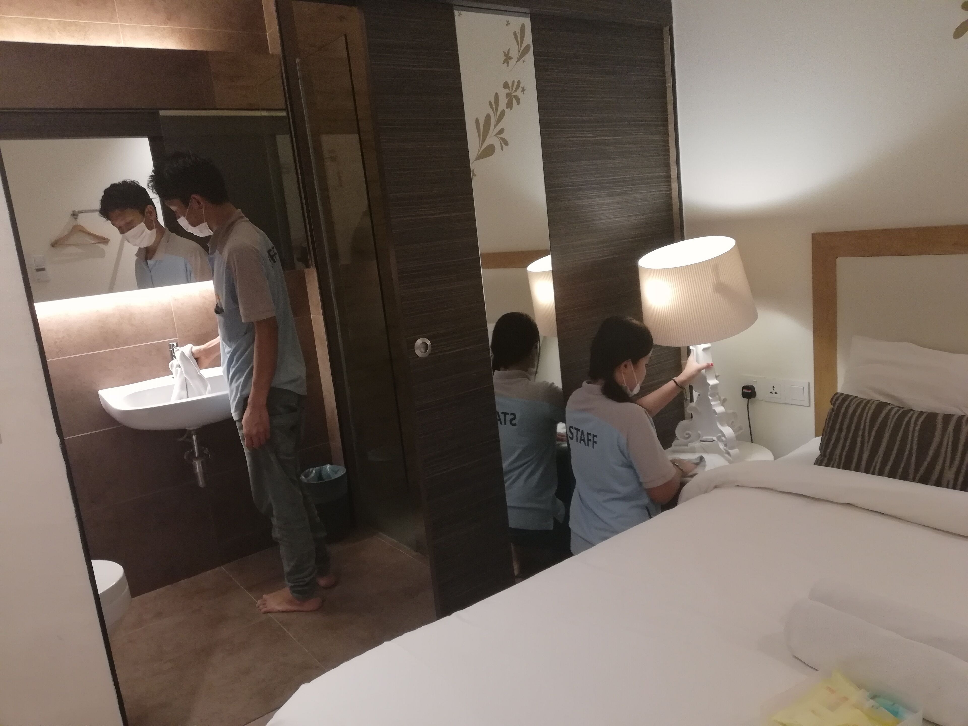 A hotel room with a bed, a bedside table with a lamp, a bathroom with a sink, and a mirror.