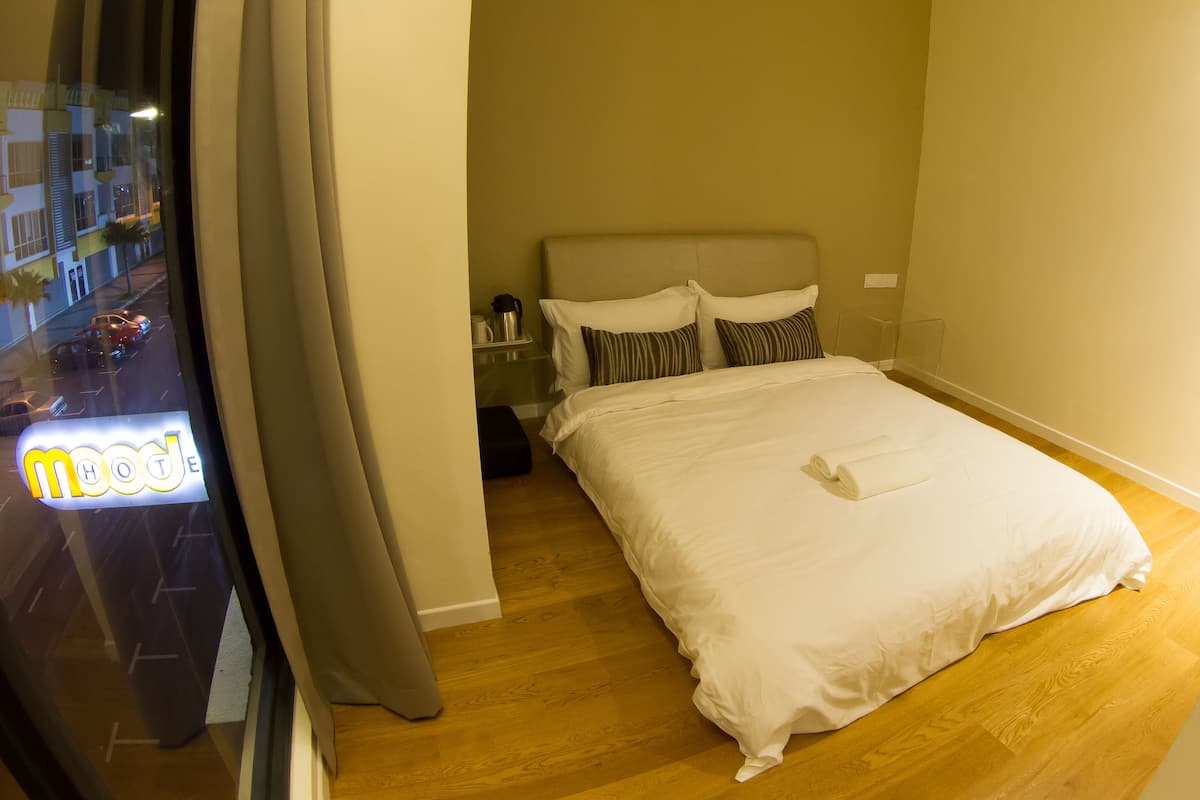 A hotel room with a bed, a nightstand, and a window with a view of the street.