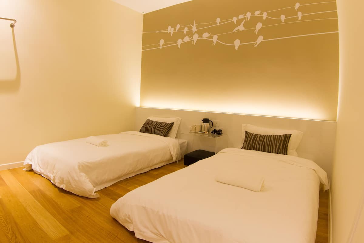 A hotel room with two single beds, a nightstand, and a wall-mounted shelf with a kettle and cups.