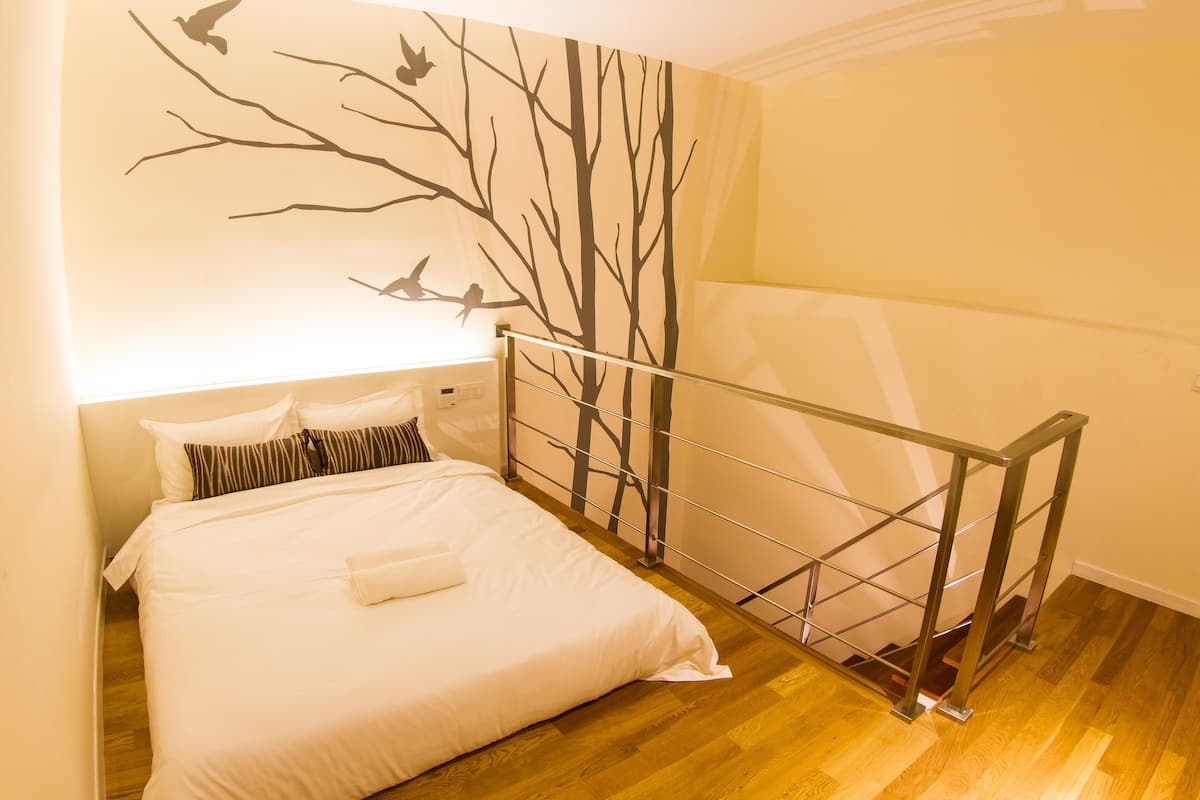 A bedroom with a bed, a railing, and a wall mural of trees and birds.