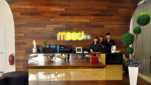 A reception desk with a wooden wall background, a neon sign, and a potted plant. - Mood Hotel (Johor Bahru)