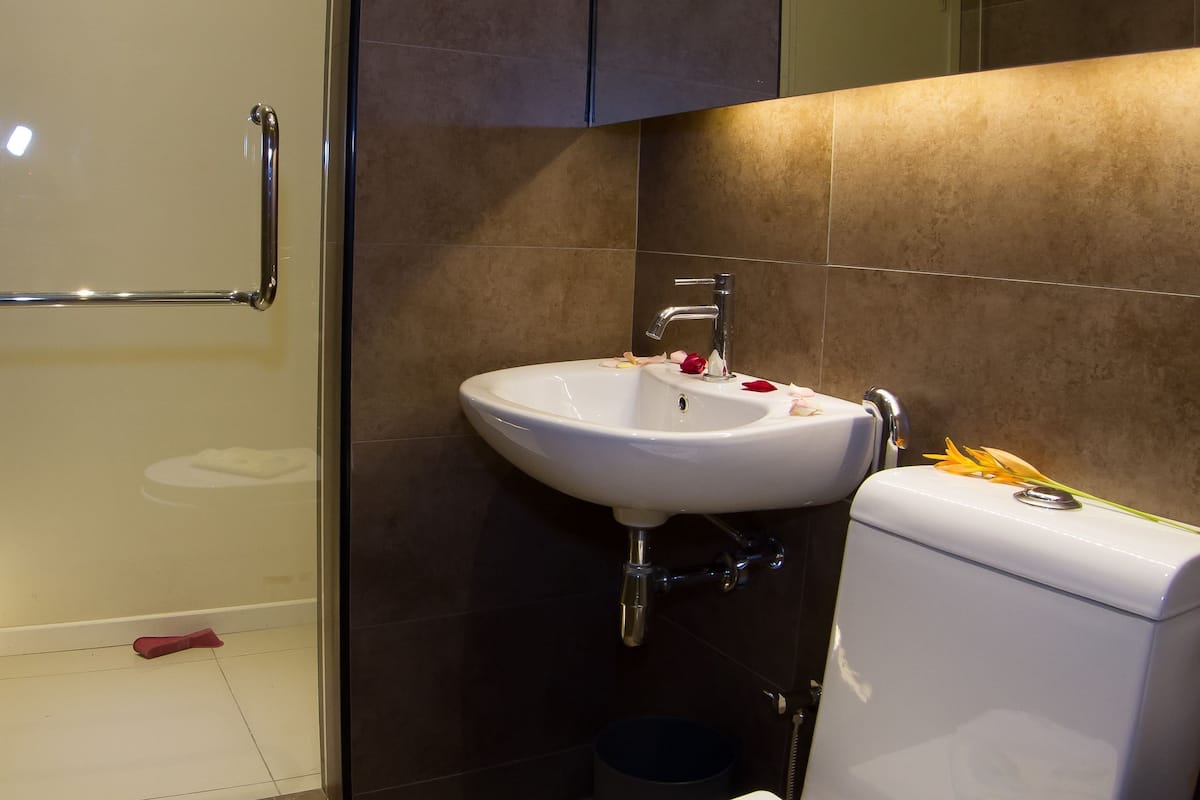 A modern bathroom with a glass shower enclosure, a white sink, and a toilet with a magazine on it.