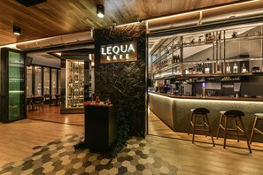 A bar area with a marble wall, wooden flooring, and a sign that reads "LEQUA CAFE".