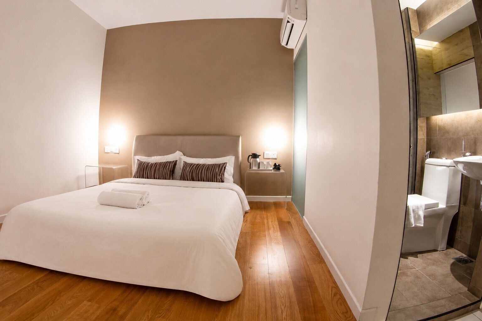 A hotel room with a bed, bedside tables, a nightstand, a mirror, and a bathroom with a sink and toilet.