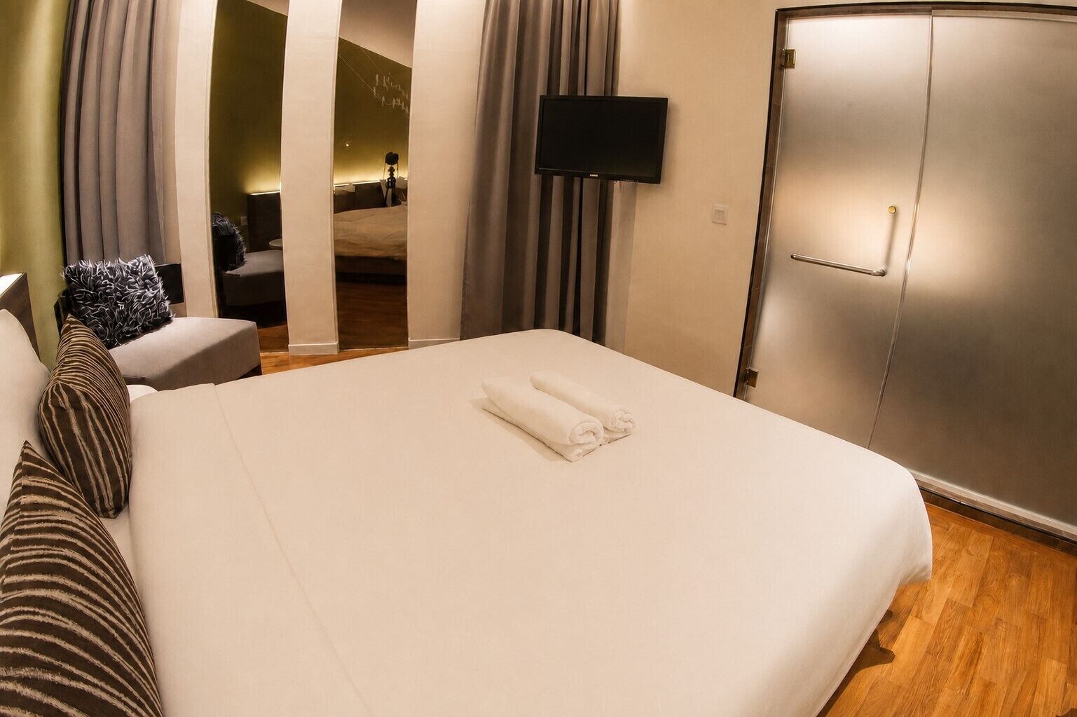 Een hotelkamer met een bed, een flatscreen televisie aan de muur, een kledingkast en een zithoek met een stoel en een bank.