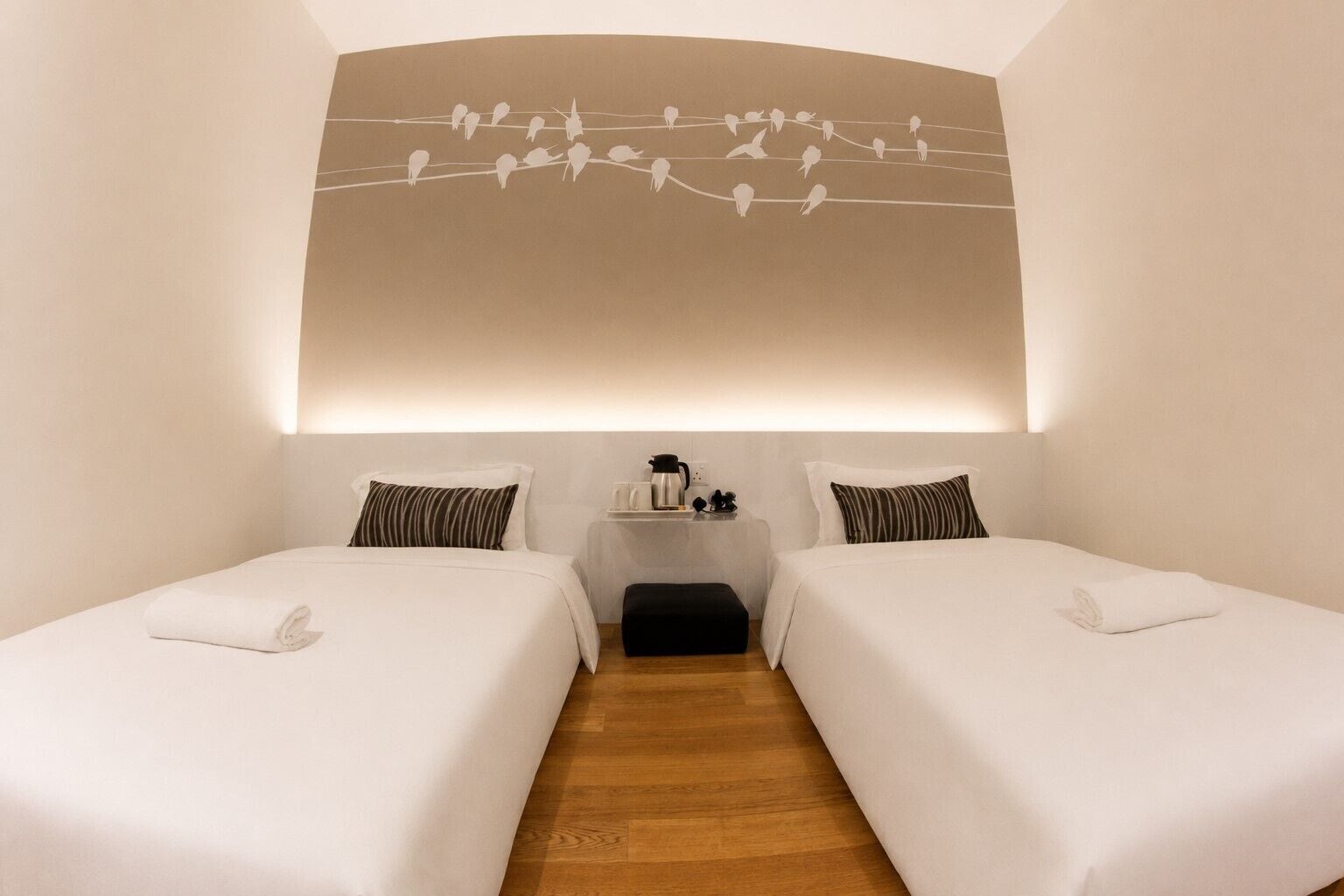 Una camera d'albergo con due letti, un tavolino con un bollitore e una decorazione a parete raffigurante degli uccelli.