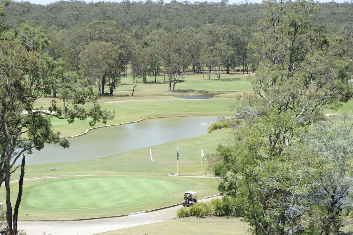 Un campo de golf con un estanque, árboles y un carrito de golf.