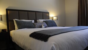 A neatly made bed with a dark headboard, white bedding, and a gray throw blanket. There are two bedside lamps on either side of the bed. - Riverside Oaks Golf Resort (Cattai)