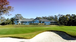 A large, modern building with a reflective glass facade, situated on a well-maintained golf course with a sand bunker in the foreground. - Riverside Oaks Golf Resort (Cattai)