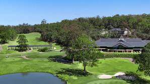 A golf course with a clubhouse, a pond, and a large house with solar panels. - Riverside Oaks Golf Resort (Cattai)