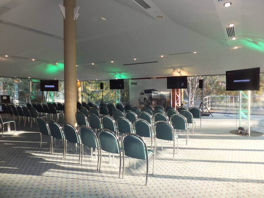A conference room with rows of chairs, a stage with a speaker, and a large screen displaying a Jeep advertisement.