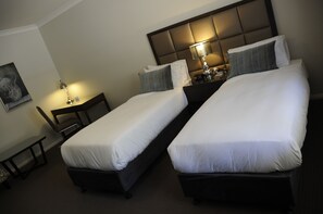 A hotel room with two single beds, a nightstand with a lamp, a chair, and a framed picture on the wall.