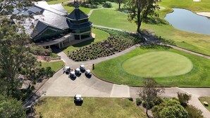 A golf course with a clubhouse, a pond, and several golf carts parked near the entrance. - Riverside Oaks Golf Resort (Cattai)