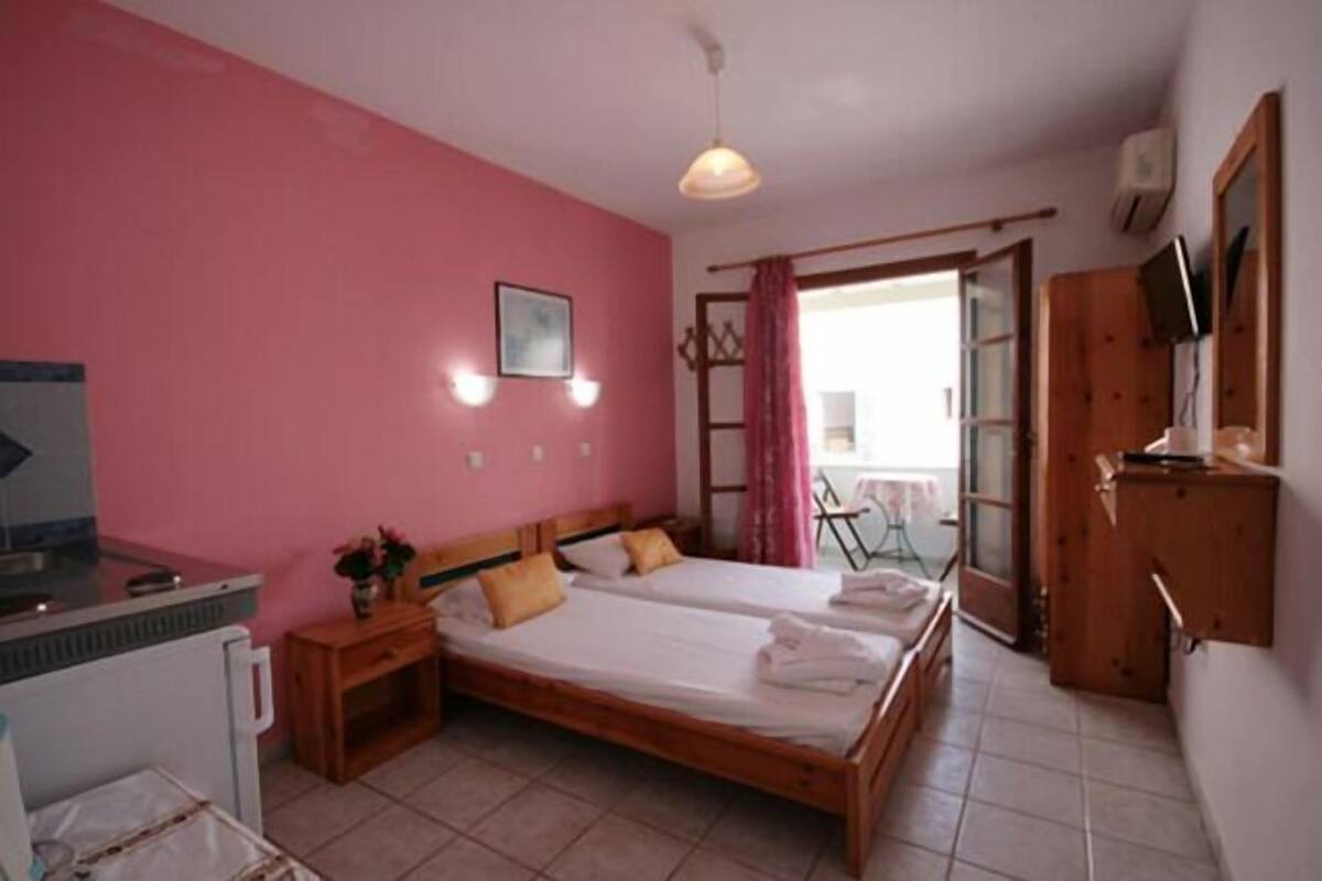 A bedroom with two beds, a small table, a desk, a chair, and a window with curtains.