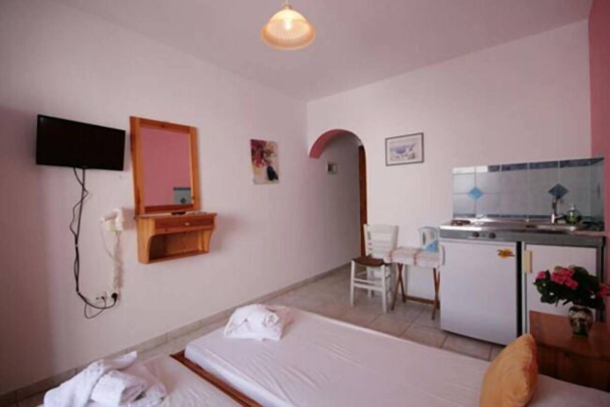 A hotel room with a bed, a desk, a chair, a small kitchenette, and a TV mounted on the wall.