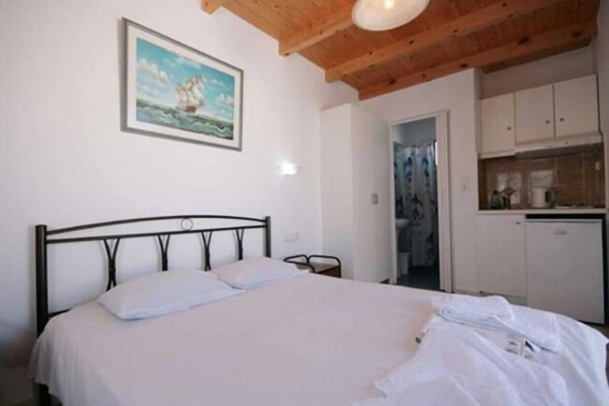 A bedroom with a bed, a painting, and a kitchenette.