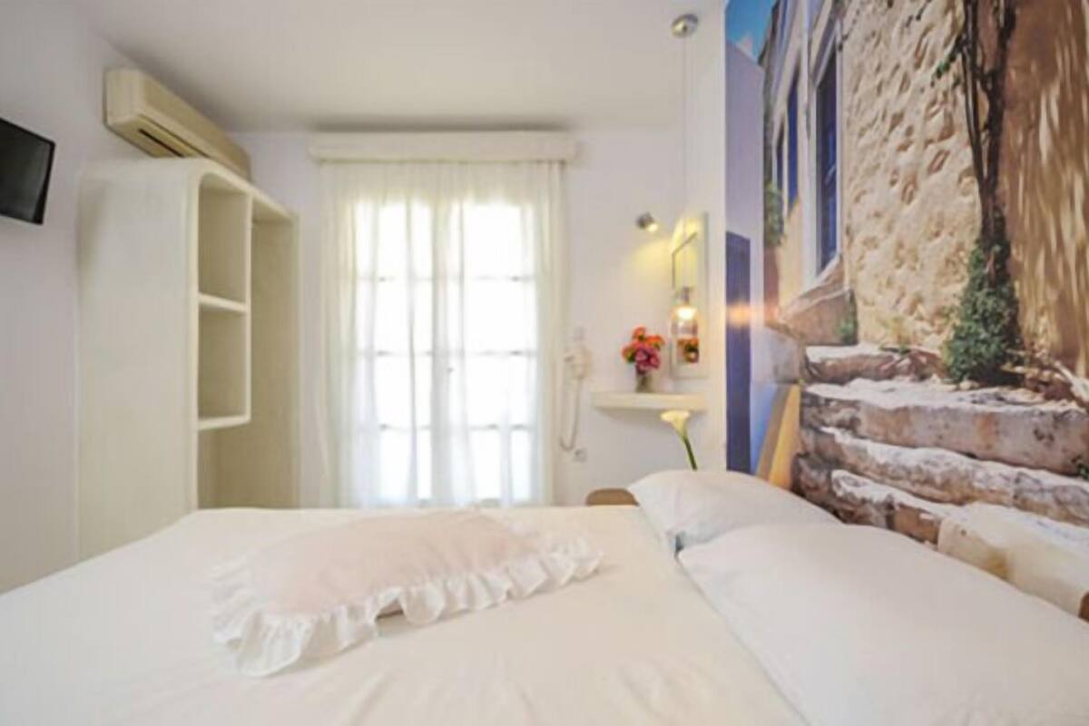 A bedroom with a bed, a wardrobe, a mirror, and a wall-mounted TV.