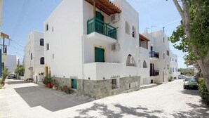 Un bâtiment blanc avec une porte et un balcon verts, entouré d’une rue étroite et de voitures garées.