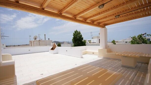 Une terrasse sur le toit avec des poutres en bois, des murs blancs et des sièges de couleur beige.