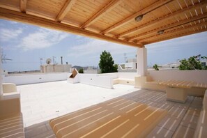 A rooftop terrace with wooden beams, white walls, and beige seating. - Studios Simos (Naxos)