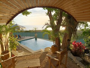 Ein Poolbereich mit Meerblick, umgeben von Holzstühlen und Kübelpflanzen.
