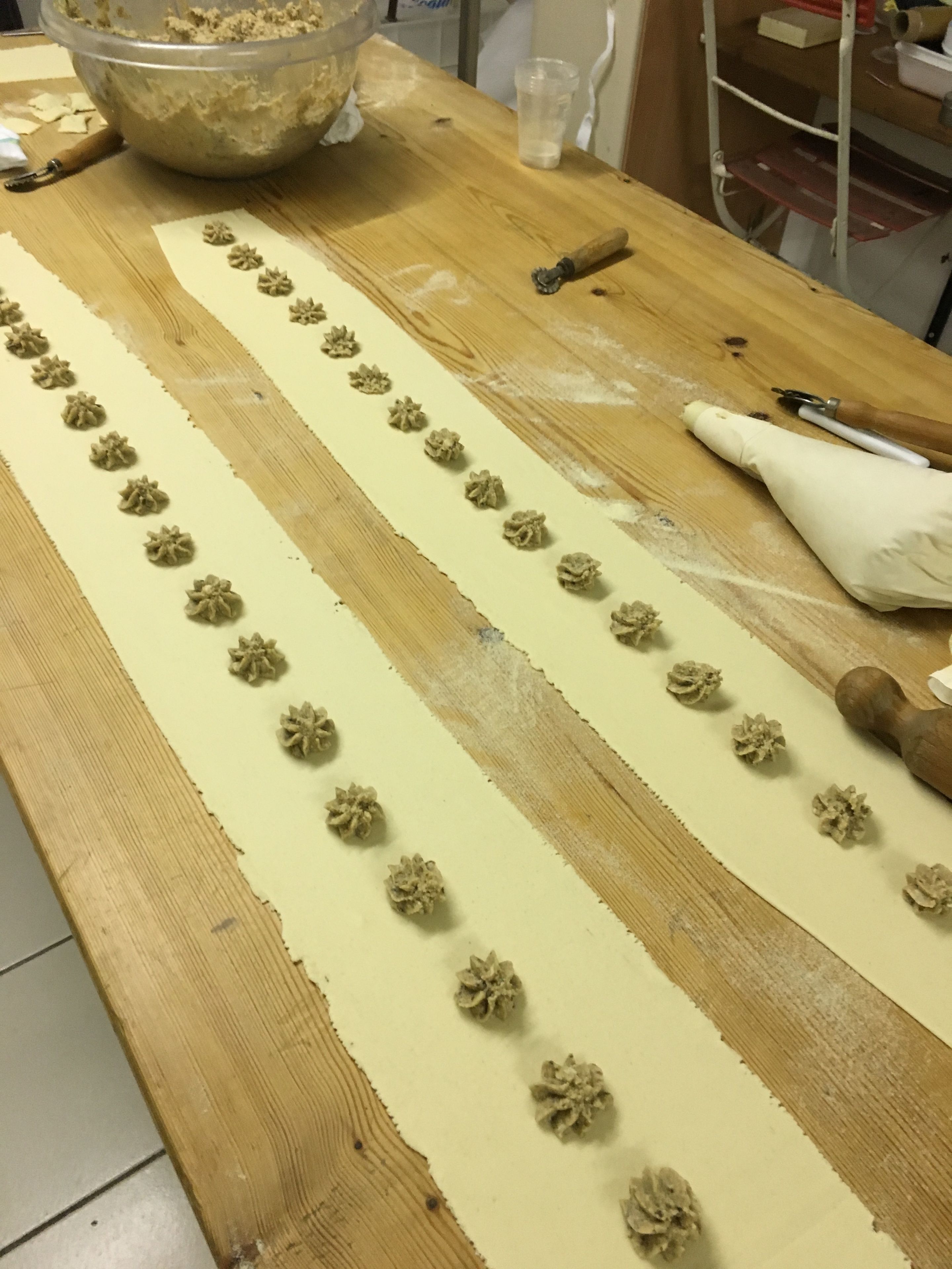 Ein Holztisch mit Teig, der zu Blumen geformt wurde, einem Nudelholz und einer Schüssel Mehl.